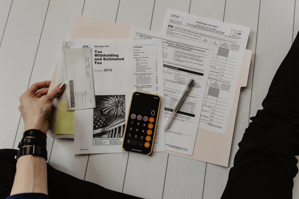 Persona con un papel en la mano junto a un bolígrafo y una calculadora